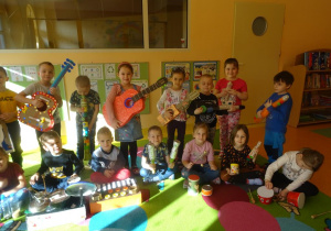 Grupa dzieci stoi lub siedzi wspólnie i pozują z instrumentami muzycznymi wykonanymi z materiałów pochodzących z recyklingu.